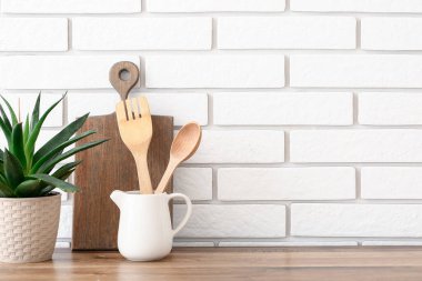 Mutfak aletleri beyaz tuğla duvarın yanındaki ahşap tezgahta.