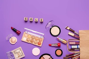 Makyaj malzemeli alışveriş çantası ve mor arka planda metin satışı