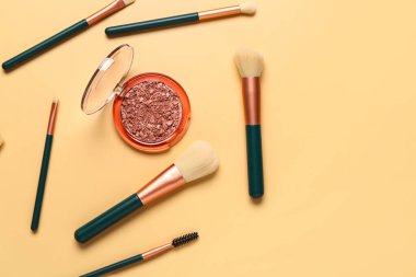 Sarı arkaplanda makyaj fırçaları ve fosforlu kalemler