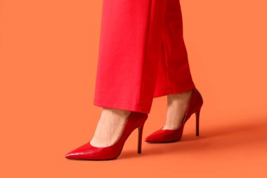 Turuncu arka planda kırmızı topuklu genç bayanın bacakları.