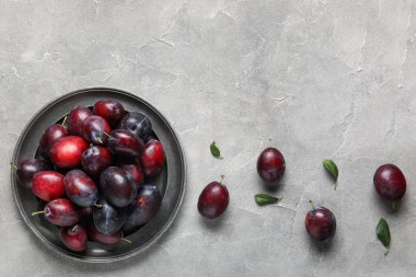 Taze erik ve gri arkaplanda yapraklarla dolu bir tabak.