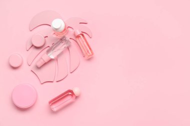 Farklı kozmetik ürünleri ve pembe arka planda dekoratif palmiye yaprağı içeren kompozisyon