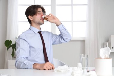 Hasta işadamı ofiste burun damlası kullanıyor.