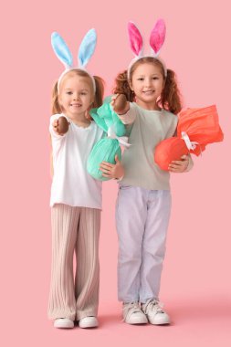 Pembe arka planda çikolatalı yumurtaları olan tavşan kulaklı şirin küçük kızlar.