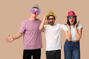 Kahverengi arka planda parti düdükleriyle kılık değiştirmiş genç arkadaşlar. 1 Nisan kutlamaları