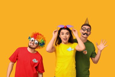 Sarı arka planda kağıt balıklarıyla komik kılık değiştirmiş genç arkadaşlar. 1 Nisan kutlamaları