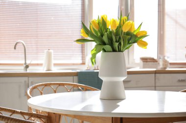 Yemek masası ve vazoda sarı laleler olan şık bir mutfak.