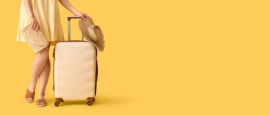 Sarı arka planda bavulu ve şapkası olan genç bir kadın. Mesaj için yeri var. Seyahat kavramı