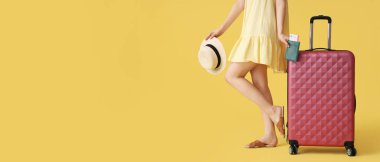 Bavulu, pasaportu ve sarı arka planda şapkası olan mesaj için yeri olan genç bir kadın. Seyahat kavramı