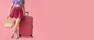 Pembe arka planda bavulu ve plaj çantasıyla mesaj için yeri olan genç bir kadın. Seyahat kavramı
