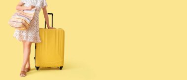 Sarı arka planda bavulu ve plaj çantasıyla mesajlaşmak için yeri olan genç bir kadın. Seyahat kavramı
