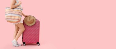 Bavulu, şapkası ve plaj çantasıyla pembe arka planda mesaj atmak için yeri olan genç bir kadın. Seyahat kavramı