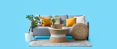 Hasır sehpası ve mavi arka planı olan rahat gri kanepe.