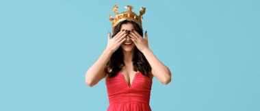 Şık balo elbisesi ve açık mavi arka planda taç giymiş güzel bir genç kız.