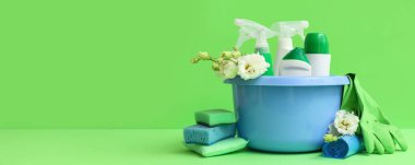 Temizlik malzemeleri ve yeşil arka planda bahar çiçekleriyle dolu bir leğen.