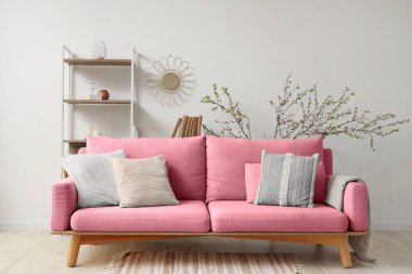 Oturma odasının içinde kanepe, raf ünitesi ve çiçek açan dallar var.