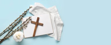 Wooden cross, pussy willow branches, Easter cake and blank book on light blue background with space for text, top view