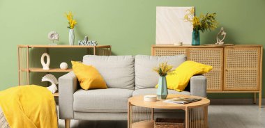 Gri kanepe ve vazolarda mimoza çiçekleri olan oturma odasının içinde.