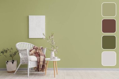 Yeşil duvarın yanındaki masada çiçek açan ağaç dalları olan beyaz koltuk ve vazo. Farklı renk desenleri