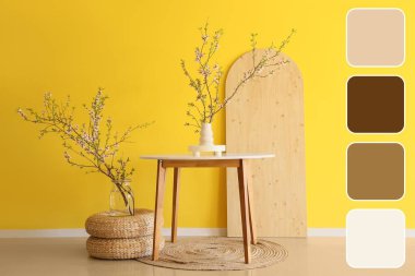 Çiçek açan dalları ve sarı duvarın yanındaki masalı vazolar. Farklı renk desenleri