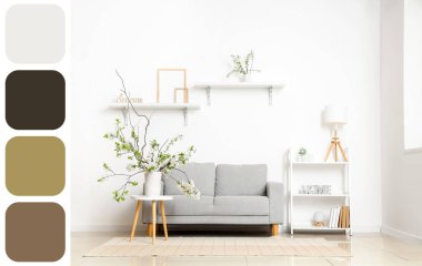 Aydınlık oturma odasındaki gri kanepenin yanındaki masada çiçek açan ağaç dalları olan vazo. Farklı renk desenleri