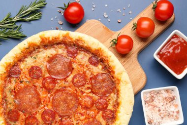 Board with delicious pepperoni pizza and ingredients on blue background