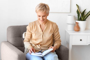 Evde kitap okuyan olgun bir kadın.