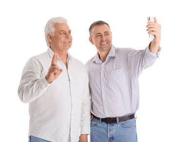 Cep telefonlu olgun kardeşler beyaz arka planda selfie çekiyorlar.