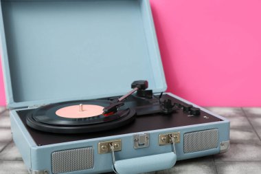 Pembe duvarın yanındaki masada vinil diski olan kayıt çalar