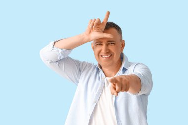 Olgun adam mavi arka planda ezik jesti gösteriyor