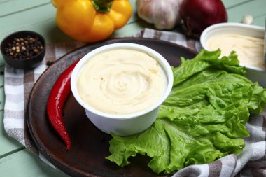 Yeşil ahşap arka planda işlenmiş peynir ve sebzelerle dolu bir tabak.