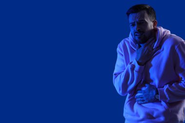 Genç adam mavi arka planda panik atak geçiriyor.