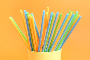 Turuncu arka planda farklı renkli pipetleri olan fincan