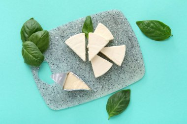 Turkuaz arka planda lezzetli işlenmiş peynir ve fesleğen yaprakları olan tahta