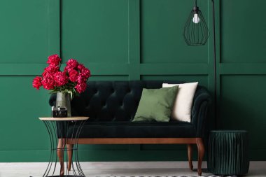 Sehpalı kırmızı şakayık vazosu, kanepe ve yer lambası yeşil duvarın yanında.