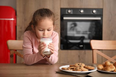 Küçük kız mutfakta süt içiyor.