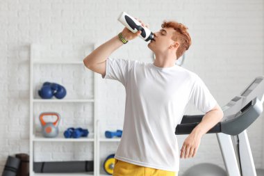 Genç kızıl saçlı adam beden eğitiminden sonra su içiyor.