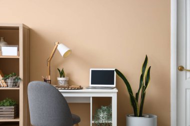 Renk duvarının yanında modern dizüstü bilgisayarı ve lambası olan rahat bir iş yeri