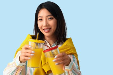 Mavi arka planda meyve suyu bardakları olan güzel Asyalı kadın.