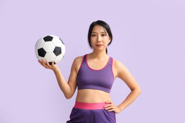 Mor arka planda futbol topu olan genç Asyalı kadın.
