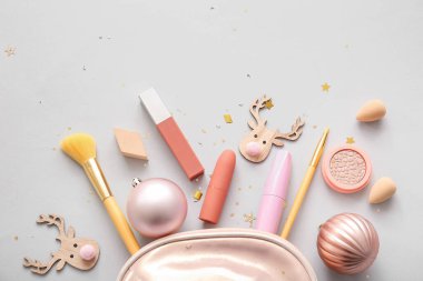 Makyaj ürünleri ve gri arka planda Noel dekoru olan kozmetik çanta.