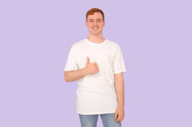 Beyaz tişörtlü genç adam leylak arka planda baş parmağını gösteriyor.