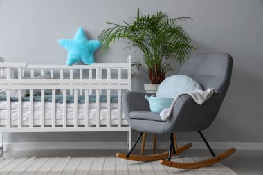 Beyaz duvarın yanında beşik ve sallanan sandalyeli çocuk odasının içi.