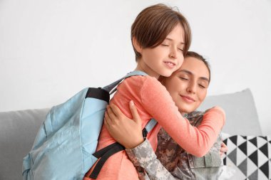 Askeri anne oğlunu kucaklıyor ve oturma odasında okula hazırlıyor.