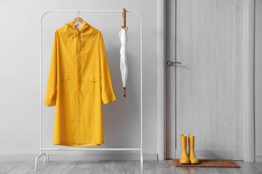 Renkli yağmurluk, şemsiye ve lastik çizmelerle aydınlık duvarın yanına dizilin.