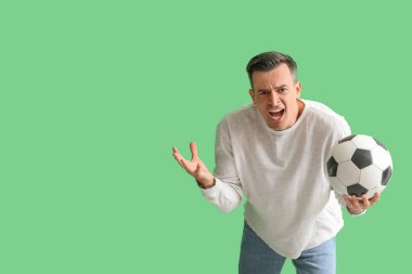 Yeşil arka planda futbol topu olan kızgın genç bir adam.