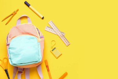 Sarı arka planda farklı kırtasiye malzemelerinin bulunduğu şık bir okul çantası.