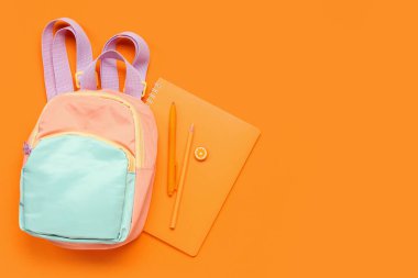 Turuncu arka planda farklı kırtasiye malzemesi içeren şık bir okul çantası.