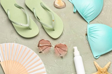 Bir şişe güneş kremi ve yeşil arka planda plaj aksesuarları.