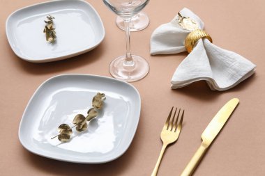 Altın çatal bıçak, yapraklar ve bej masa peçetesiyle şık bir masa.